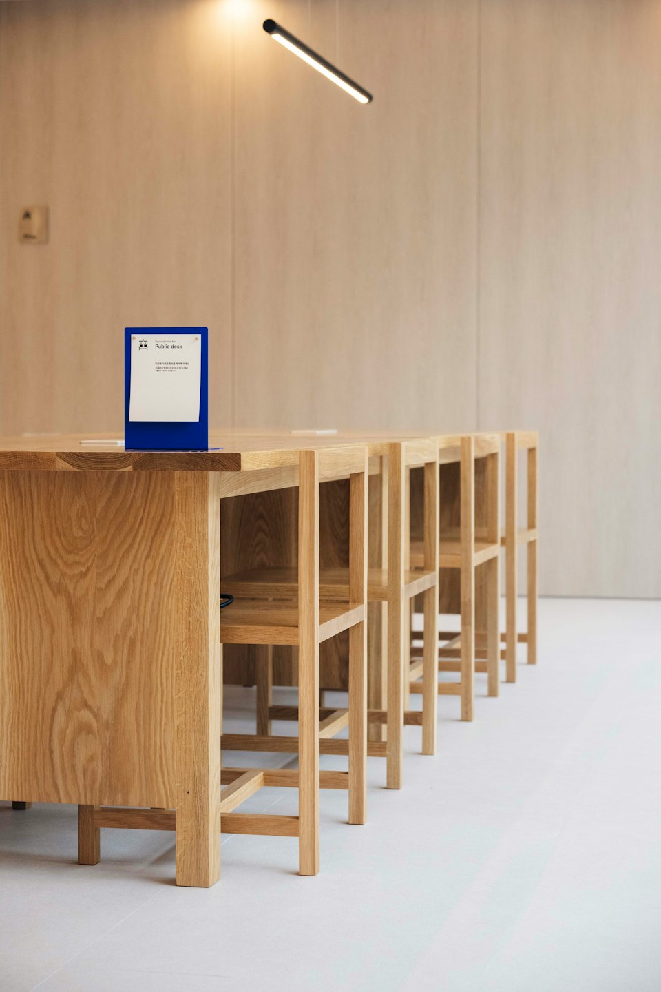 Modern public desk with wooden stools against a beige wall.